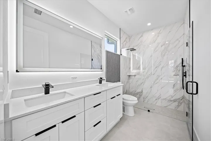 Full bath featuring a marble finish shower, double vanity, and recessed lighting