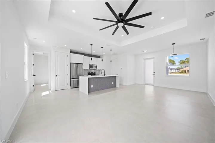 Unfurnished living room featuring ceiling fan, a raised ceiling, and recessed lighting