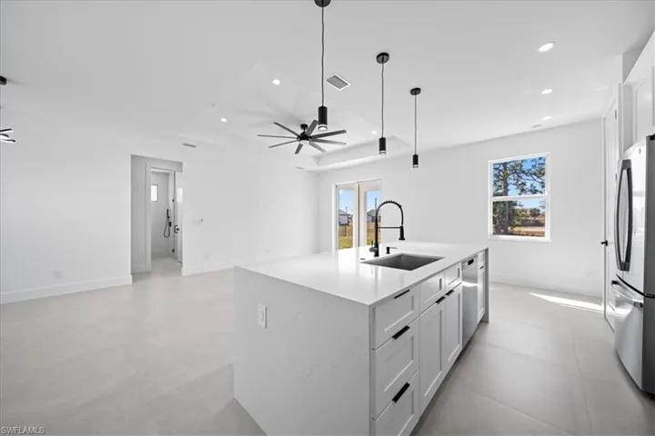 Kitchen featuring a center island with sink, light stone counters, stainless steel appliances, white cabinets, and open floor plan