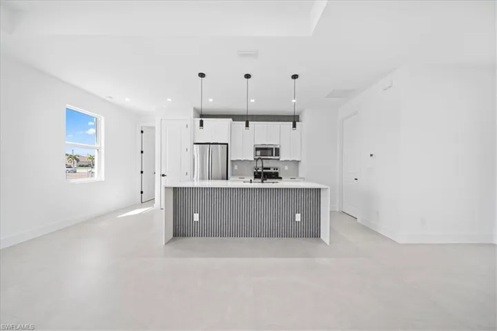 Kitchen featuring a center island with sink, white cabinetry, stainless steel appliances, hanging light fixtures, and light stone countertops