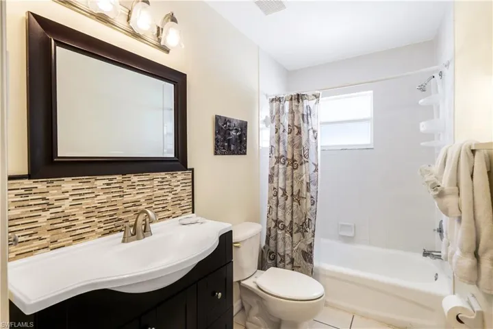 Full bathroom featuring vanity, shower / bath combo, tile patterned flooring, toilet, and tasteful backsplash