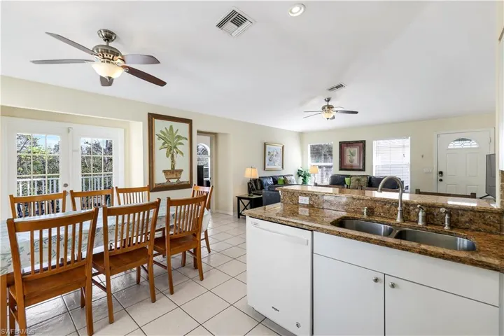Kitchen with sink, light tile patterned flooring, dark stone countertops, white dishwasher, and white cabinets