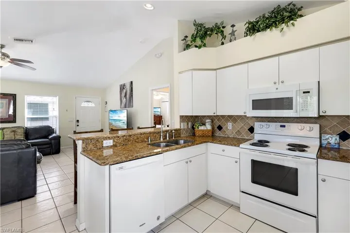 Kitchen with kitchen peninsula, white cabinetry, sink, and white appliances