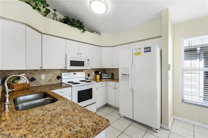 Kitchen featuring kitchen peninsula, tasteful backsplash, white appliances, sink, and white cabinetry