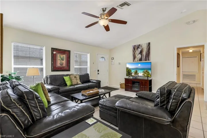 Living room with ceiling fan, light tile patterned floors, and lofted ceiling