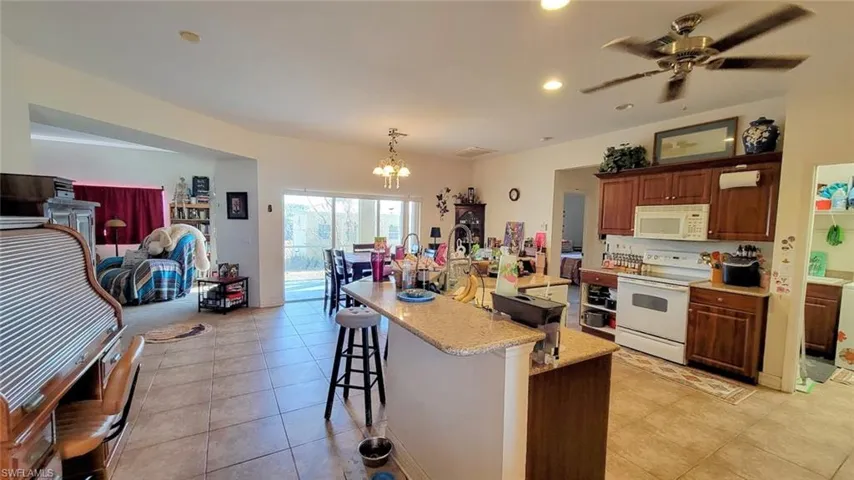 Kitchen featuring a kitchen breakfast bar, white appliances, a ceiling fan, a kitchen island with sink, and hanging lights