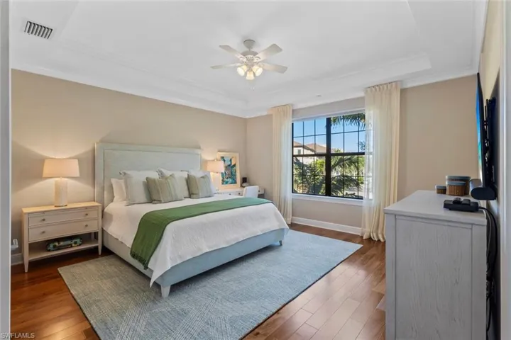 Bedroom featuring hardwood / wood-style floors, crown molding, a tray ceiling, and ceiling fan