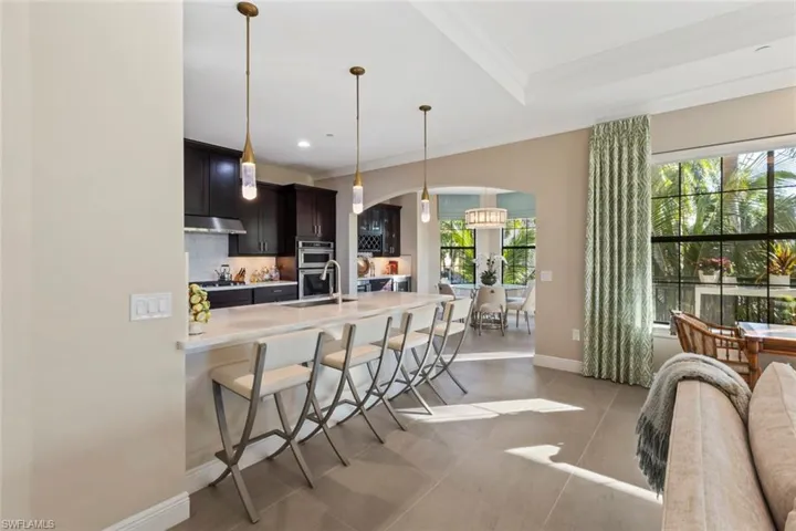 Kitchen with a breakfast bar, decorative light fixtures, light stone counters, ornamental molding, and stainless steel double oven