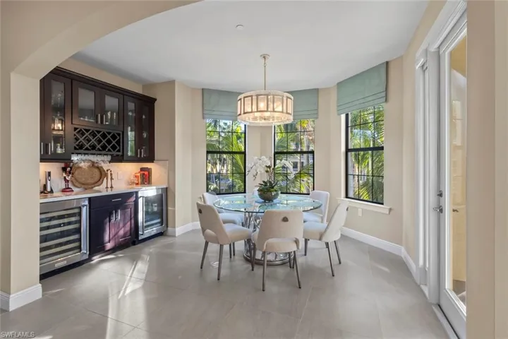 Indoor bar featuring glass insert cabinets, beverage cooler, decorative light fixtures, and light stone countertops