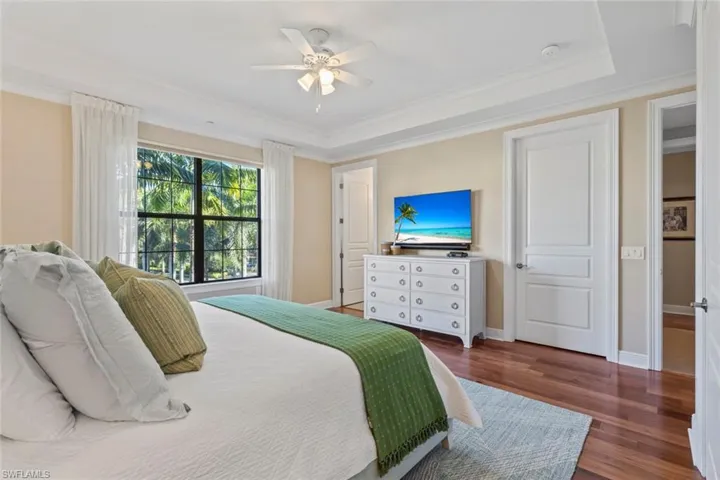 Bedroom featuring dark wood-style flooring, ornamental molding, a tray ceiling, and a ceiling fan