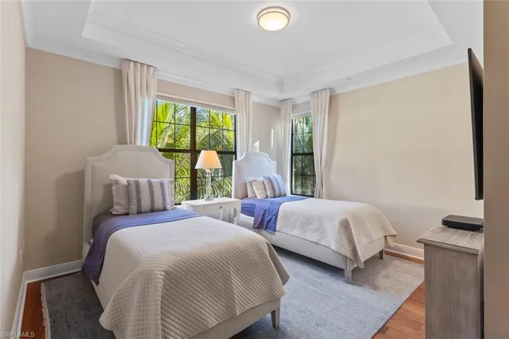 Bedroom with wood finished floors, a tray ceiling, and crown molding