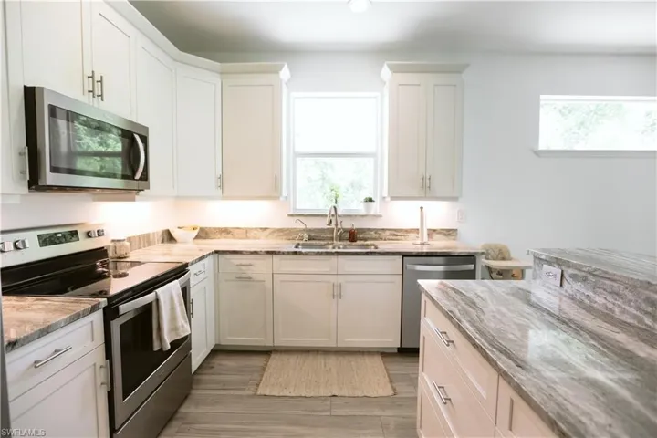 Kitchen with stainless steel appliances, a sink, light stone countertops, white cabinetry, and light wood-style floors