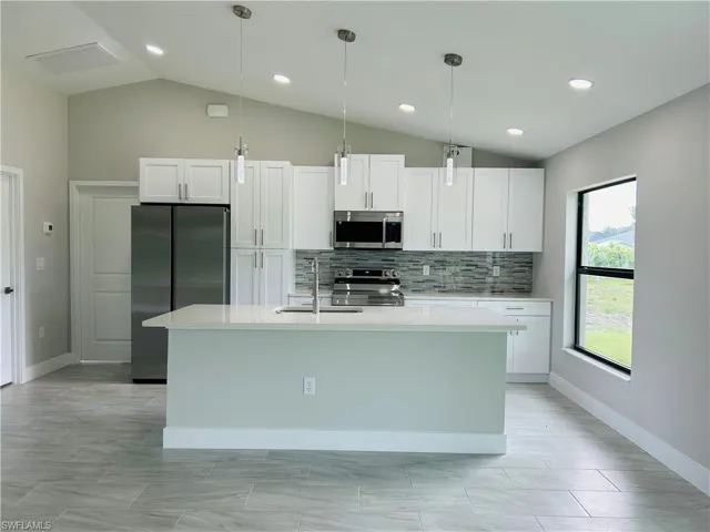 Kitchen with appliances with stainless steel finishes, hanging light fixtures, vaulted ceiling, an island with sink, and white cabinets