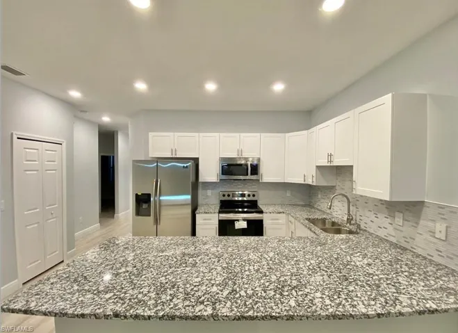 Modern kitchen with white cabinetry, stainless steel appliances, speckled stone countertops, and a full tile backsplash