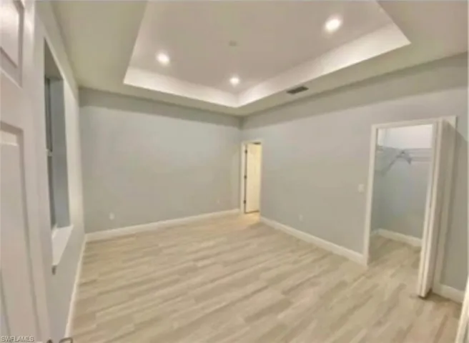 Recessed lighting, tray ceiling, light wood-finish flooring, and white trim
