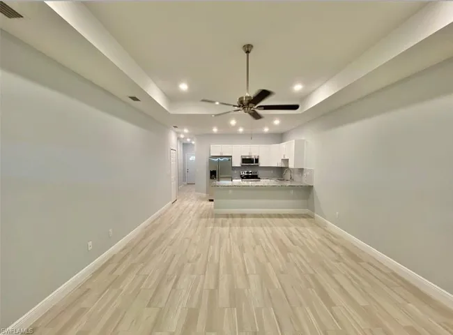 Tray ceiling with recessed lighting, wood-finish flooring, and a ceiling fan