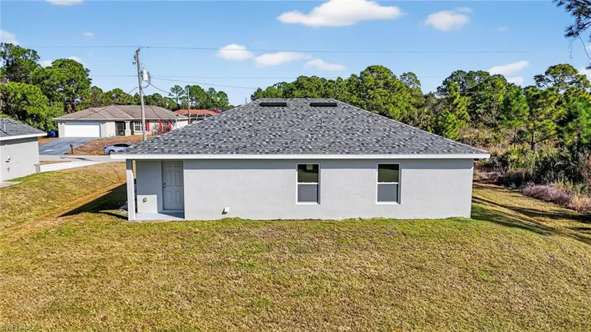 View of side of home featuring stucco siding, a lawn, and roof with shingles