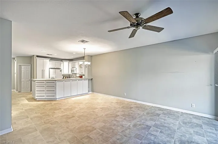 Kitchen with white cabinets, stainless steel fridge, hanging light fixtures, ceiling fan with notable chandelier, and light tile patterned flooring