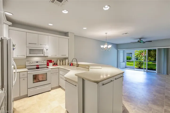 Kitchen with white appliances, kitchen peninsula, decorative light fixtures, ceiling fan with notable chandelier, and light tile patterned flooring
