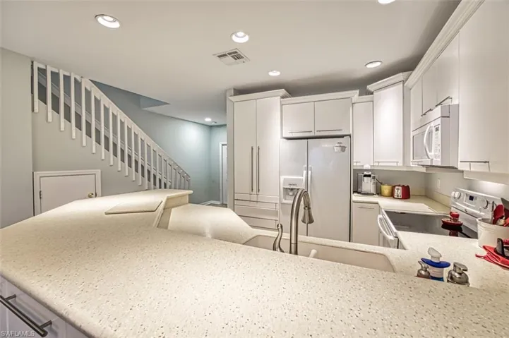Kitchen with sink, white cabinetry, kitchen peninsula, and white appliances