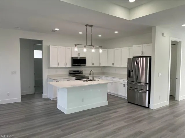 Kitchen with appliances with stainless steel finishes, recessed lighting, white cabinets, pendant lighting, and a center island with sink
