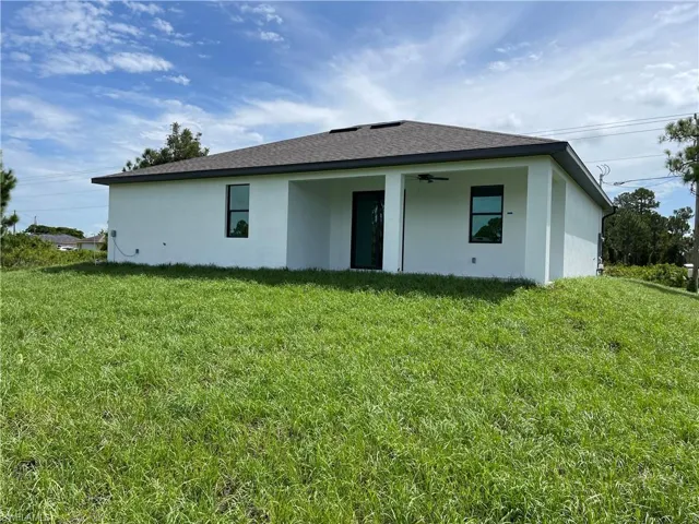 Back of house with stucco siding, a lawn, a shingled roof, and ceiling fan