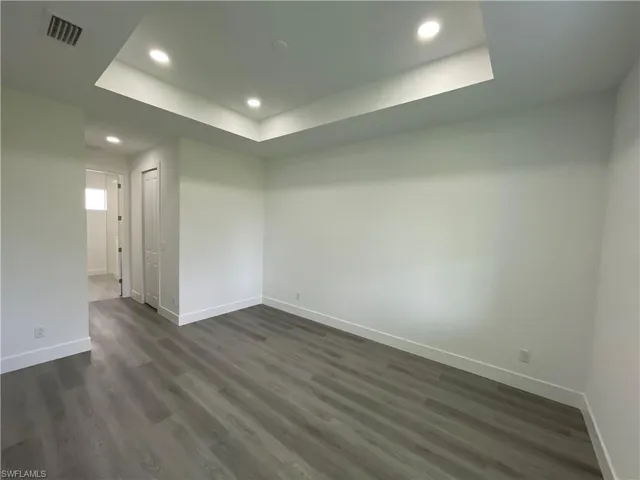 Empty room featuring a raised ceiling, dark wood-style flooring, and recessed lighting