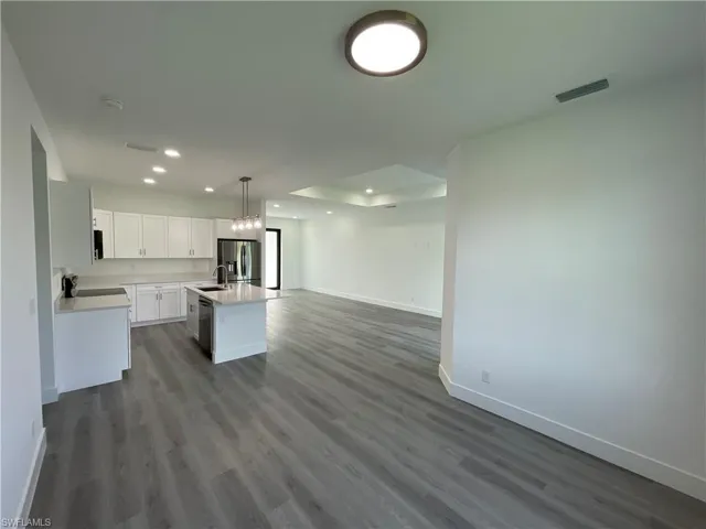 Kitchen with open floor plan, pendant lighting, white cabinetry, dark wood-type flooring, and a kitchen island with sink