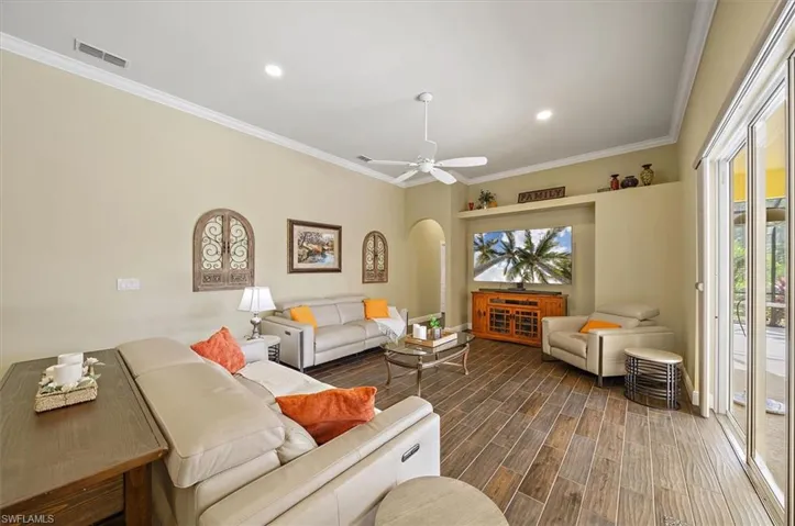 Living room with arched walkways, visible vents, plenty of natural light, and ornamental molding