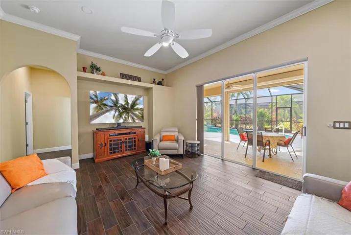 Living room featuring crown molding, a sunroom, a ceiling fan, baseboards, and wood finished floors