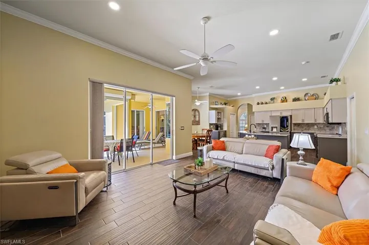 Living room featuring visible vents, crown molding, ceiling fan, and arched walkways
