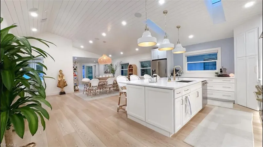 Kitchen featuring a kitchen bar, white cabinets, a center island with sink, hanging light fixtures, and light wood finished floors