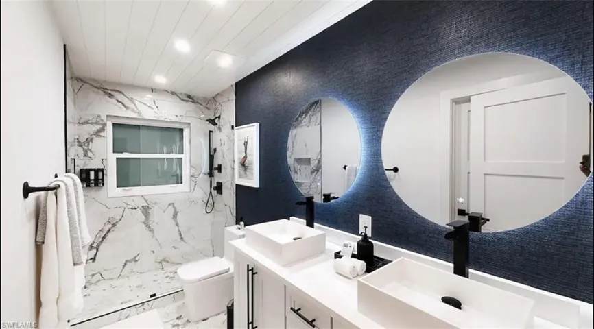 Bathroom featuring double vanity, a marble finish shower, and recessed lighting