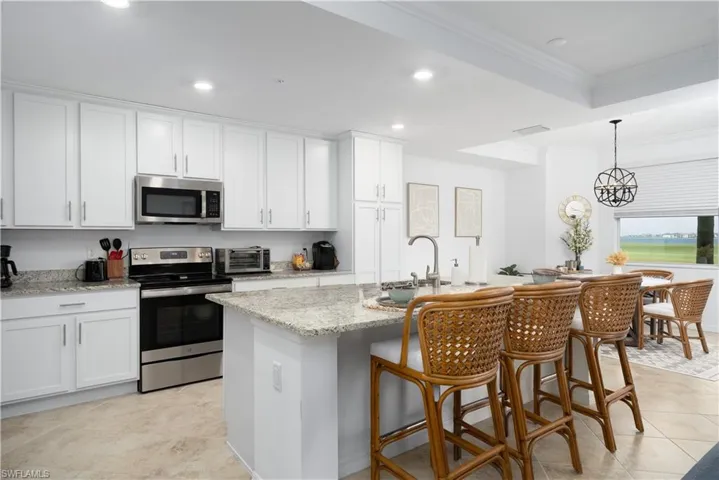 Kitchen with white cabinets, appliances with stainless steel finishes, light stone counters, and crown molding
