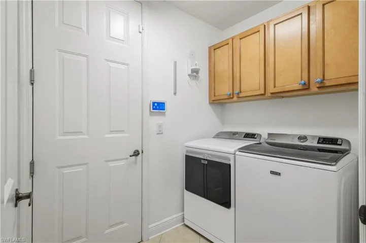 Washroom with light tile patterned floors, baseboards, cabinet space, and washing machine and clothes dryer