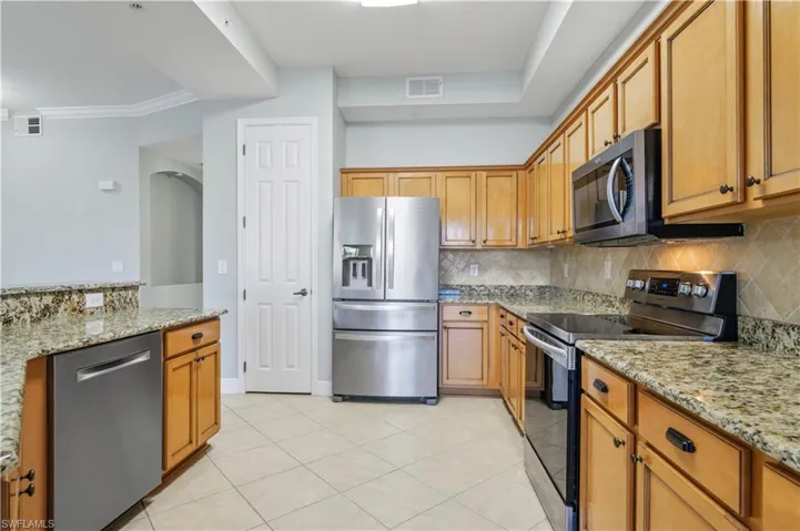 Kitchen featuring light stone counters, backsplash, visible vents, and appliances with stainless steel finishes