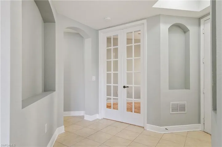Corridor with visible vents, baseboards, french doors, arched walkways, and tile patterned floors