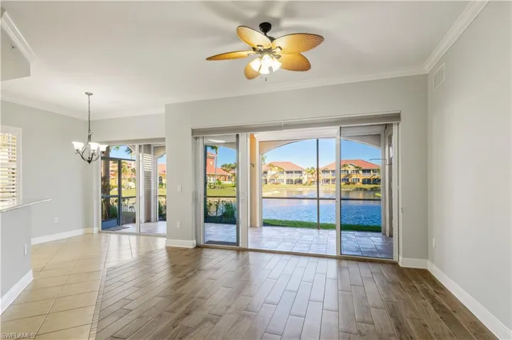Spare room featuring wood finished floors, baseboards, visible vents, ornamental molding, and ceiling fan with notable chandelier
