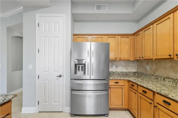 Kitchen with visible vents, stainless steel refrigerator with ice dispenser, light tile patterned floors, decorative backsplash, and light stone countertops