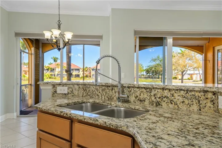 Kitchen with a chandelier, ornamental molding, light stone counters, and a sink