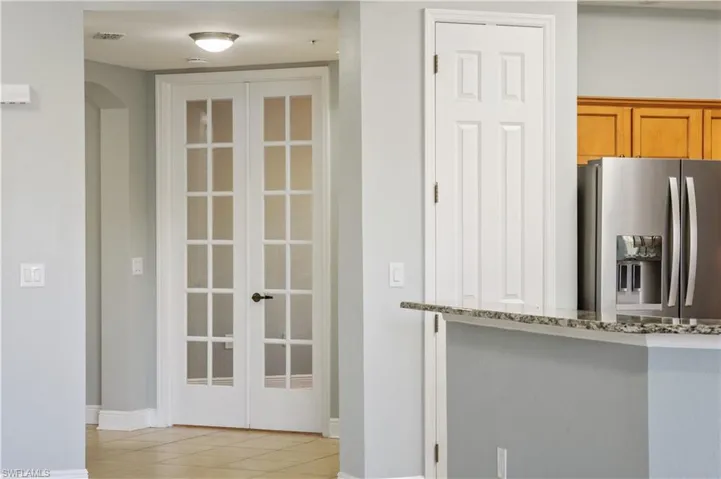 Kitchen with stainless steel refrigerator with ice dispenser, french doors, brown cabinetry, stone counters, and light tile patterned floors