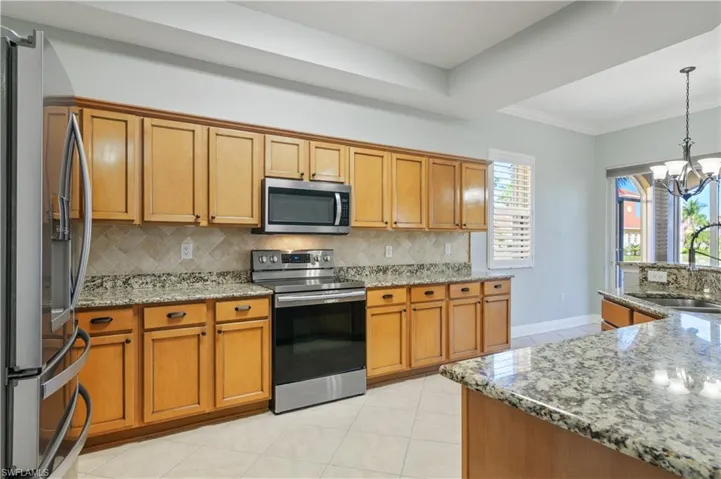 Kitchen with a notable chandelier, a sink, stainless steel appliances, brown cabinetry, and decorative backsplash