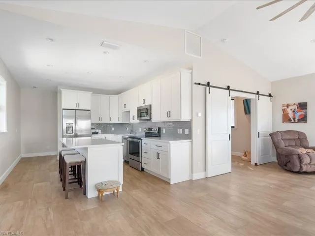 Kitchen with a barn door, open floor plan, stainless steel appliances, white cabinets, and a center island