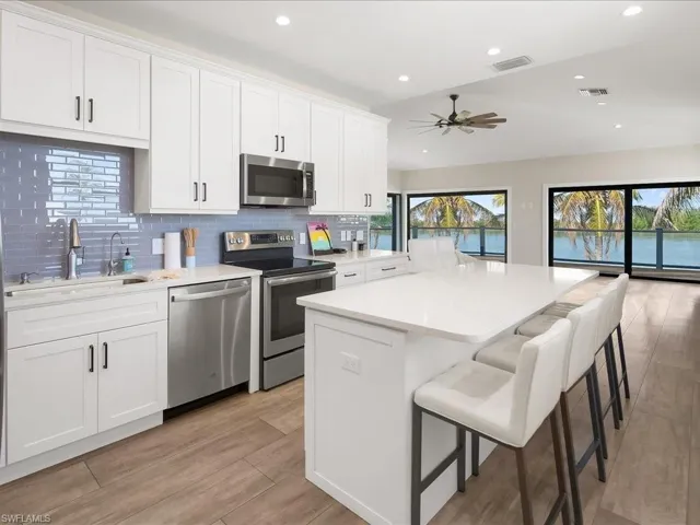 Kitchen with stainless steel appliances, white cabinetry, light wood finished floors, a center island, and backsplash