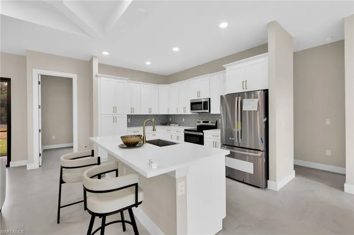 Kitchen with stainless steel appliances, white cabinets, recessed lighting, an island with sink, and a kitchen breakfast bar