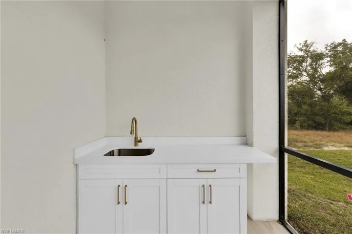 Bar area featuring a textured wall, white cabinets, and light stone countertops