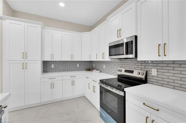 Kitchen featuring appliances with stainless steel finishes, white cabinetry, light stone counters, backsplash, and light marble finish flooring