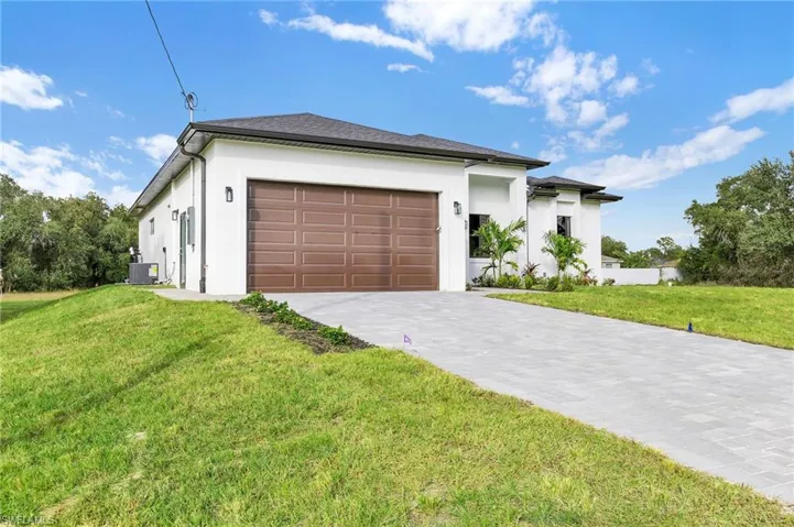 Prairie-style home featuring an attached garage, decorative driveway, a front yard, and stucco siding