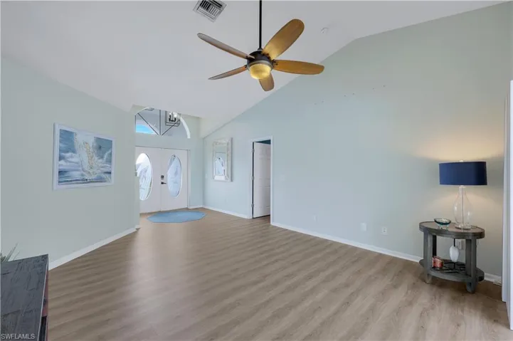 Unfurnished living room with french doors, ceiling fan with notable chandelier, high vaulted ceiling, and light hardwood / wood-style flooring