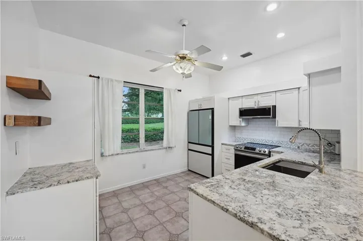 Kitchen with open shelves, light stone counters, decorative backsplash, white cabinetry, and stainless steel appliances